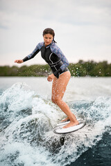 Beautiful woman in swimsuit stands on a surfboard and rides on splashing wave