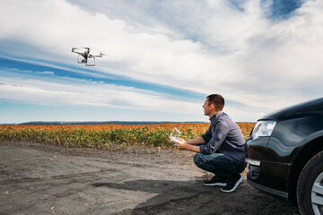 A man standing near the car launches a drone. drone flight in yellow field
