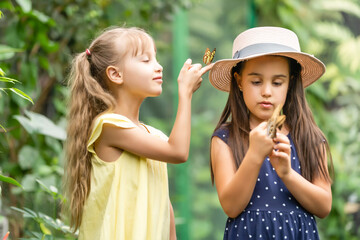 Two little sisters holding a butterfly in their hands. Children exploring nature. Family leisure...