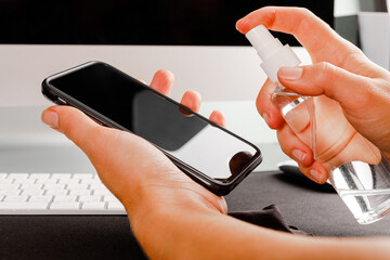 Woman Wiping Mobile Phone Screen With Sanitizer on wood background. Cleaning smart phone screen to...