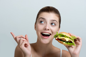 Young beautiful smilling girl holds a burger in hand and pointing to the left side.