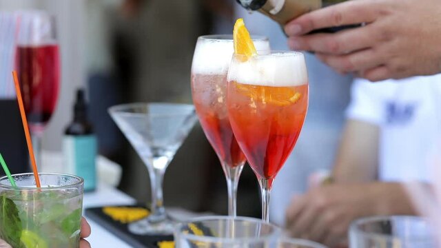 Close up, the bartender pours champagne into glasses with orange slices, and foam forms. The waiter prepares drinks for the guests.