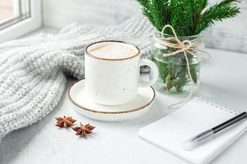 Cup of coffee, scarf, notebook and bouquet of fir tree branches. Cozy autumn or winter composition. Scandinavian style