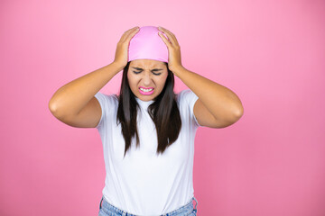 Obraz na płótnie Canvas Young beautiful woman wearing pink headscarf over isolated pink background suffering from headache desperate and stressed because pain and migraine with her hands on head