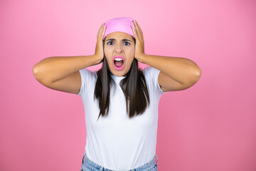 Obraz na płótnie Canvas Young beautiful woman wearing pink headscarf over isolated pink background crazy and scared with hands on head, afraid and surprised of shock