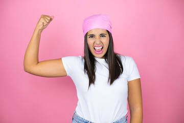 Young beautiful woman wearing pink headscarf over isolated pink background showing arms muscles smiling proud