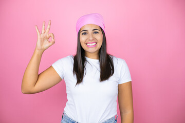 Young beautiful woman wearing pink headscarf over isolated pink background doing ok sign with fingers and smiling, excellent symbol