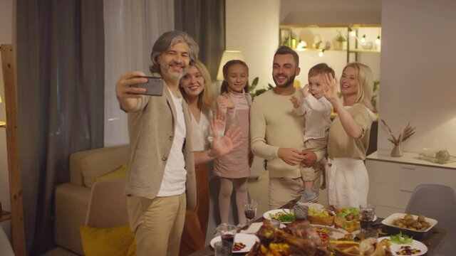 Stylish mature man holding smart phone taking selfie pictures with his family on Thanksgiving day, medium long shot footage