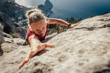 Schilderijen op glas Brave young woman climber fearlessly climbs up sheer stone wall in mountains, overcoming obstacles. Dangerous chasm balancing, adrenaline and courage in extreme sports © Komarov Dmitriy