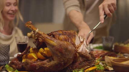 Unrecognizable mature man standing at dining table cutting roasted turkey for Thanksgiving day dinner - Powered by Adobe