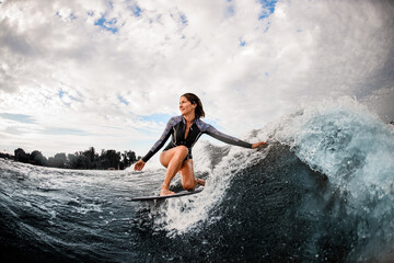 woman having fun sitting on surf board and touching the water with her hand. - obrazy, fototapety, plakaty