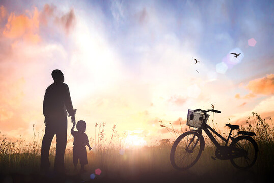 Father day concept: Silhouette child's hand holding father's hand with bicycle on meadow and sky sunset background