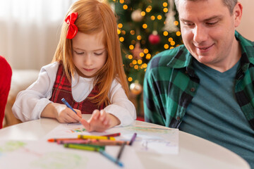 Mother, father and daughter drawing with crayons on Christmas day