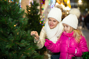 Pleasant woman with daughter buying Christmas tree in market. High quality photo