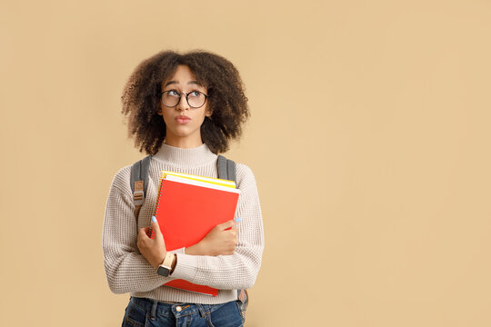 Make choices or think about study, problems at education. Pensive african american woman student in glasses with backpack holds notepads and looks up to free space