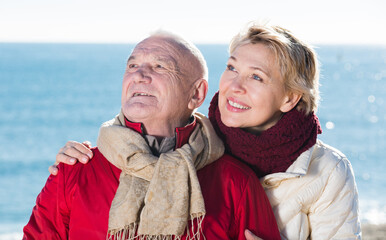 Senior couple taking walk by sea on sunny chilly day