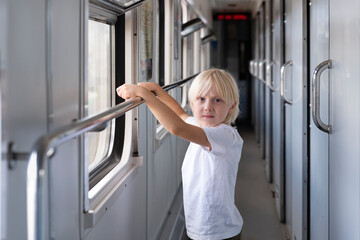 Fototapeta na wymiar Cute blond boy traveling by train. Children in railroad car.