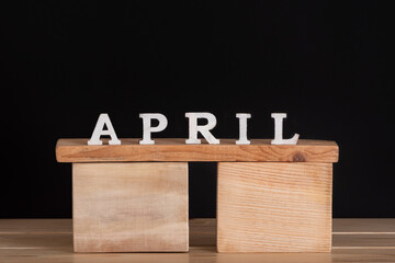 Word April written on wooden blocks. Black background. Spring calendar.
