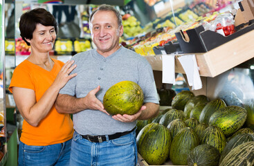 Fototapeta premium Smiling man and his wife are choosing ripe melon in the fruit store