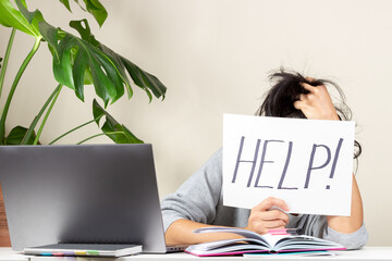 Tired frustrated woman sitting at table and holding card with word Help. Online working, learning...