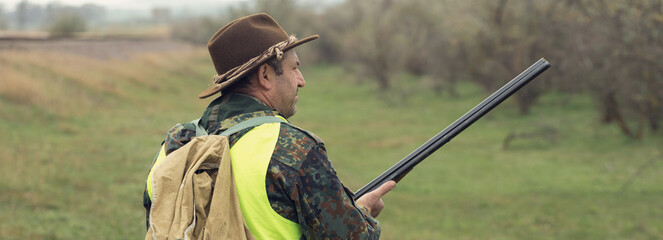 Duck hunter with shotgun walking through a meadow.