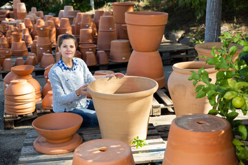 Portrait of female worker of gardening material warehouse checking and arranging big clay pots