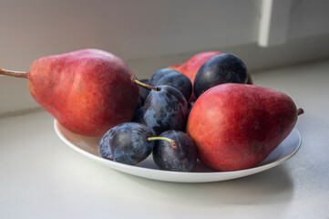 Group of pears and blue plums edible fruits, tasty ripened red yellow fruit on the table