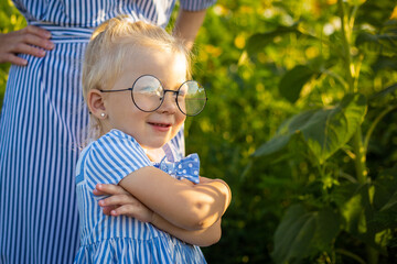 Little girl in dress and glasses and mom on a sunflower field