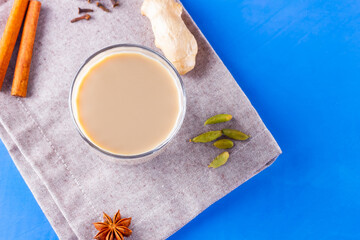Masala chai tea on a linen napkin. Traditional indian drink - masala tea with various spices. Glass of masala tea on a blue background