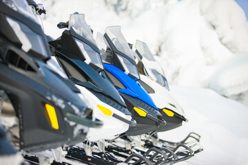 Several multi- colored snowmobiles standing in a row outdoor on a snowy background.