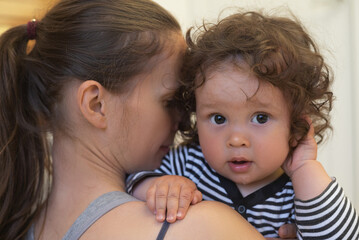 Close up portrait of a long haired adorable toddler and lovely mother holding him in her arms and embracing him.