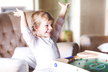 Happy little toddler girl playing table soccer with family at home. Smiling child winning board football, indoors. Indoor leisure for kids during corona virus self-isolation quarantine time.