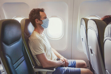 passenger wearing face mask in airplane, travel during covid 19 pandemic of coronavirus