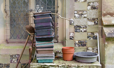 Garden trays flowerpots sieve and broom propped against church wall