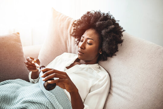 Woman disgusted of some cough syrup she has to drink to feel better. Woman taking cough syrup on sofa at home. Ill woman with grey scarf taking cough syrup