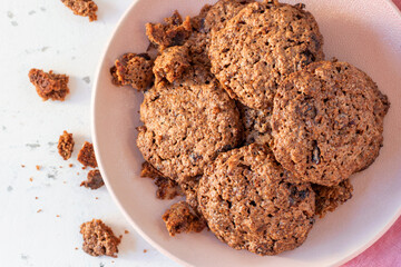 Homemade oatmeal cookies on a pink plate with crumbs.