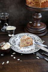 A slice of apple pie in almond flakes with a creamy sauce. Still life with dessert and vintage dishes. Dark shades.