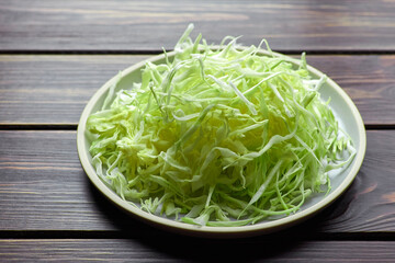 Shredded fresh green cabbage salad on ceramic plate on wooden table background.