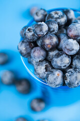 Glass filled with fresh blueberries on light blue background. Studio shot. Selective focus on subject.