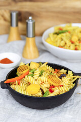 Pasta with vegetables and spices in a cast-iron frying pan.