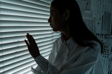 Woman looking outside the window in dark room.