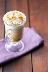 Pumpkin spice latte in a glass mug. Pumpkin latte with whipped cream and spices on a wooden boards. Hot autumn coffee drink on a linen napkin