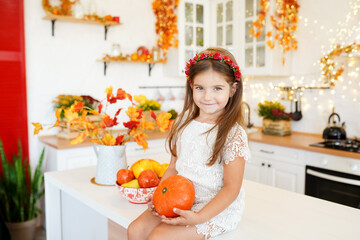 adorable little girl holding pumpkin sitting in the kitchen, thanksgiving concept