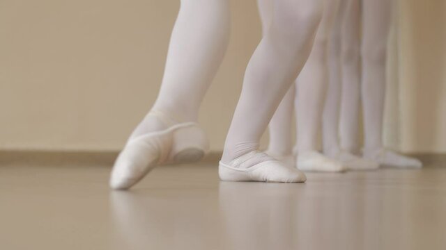 Ballerinas feet close up. Young ballerinas perform a group exercise in class. Classical ballet lessons in a ballet class on the floor. Warm up before class. Camera movement along the ballerinas.