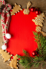 frame for Christmas greetings made of gingerbread cookies, fir twigs, red Christmas decorations. red frame background an a light brown wooden background