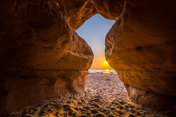 Spacious cave next to Baltic sea glowing in sunset colors. Beach sands and sea in colorful sunset.
