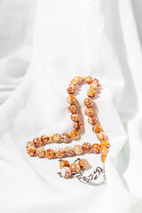 Islamic prayer beads on a white silk fabric. Design concepts on the theme of Ramadan or other Islamic religious events.