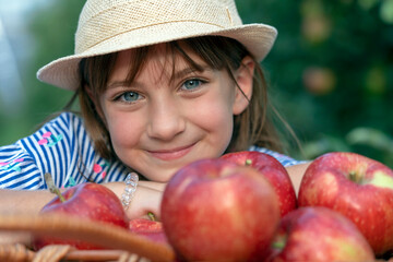 Portrait of a Smiling Blue Eyed Girl in a Straw Hat With A Basket of Red Apples