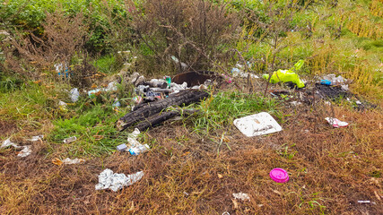 Heap of rubbish on grass in the park. Plastic and glass bottles, bottle caps and paper. Concept of environmental protection and littering of environment.