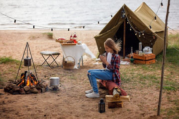 A girl in a plaid shirt and blue jeans is holding a mug.